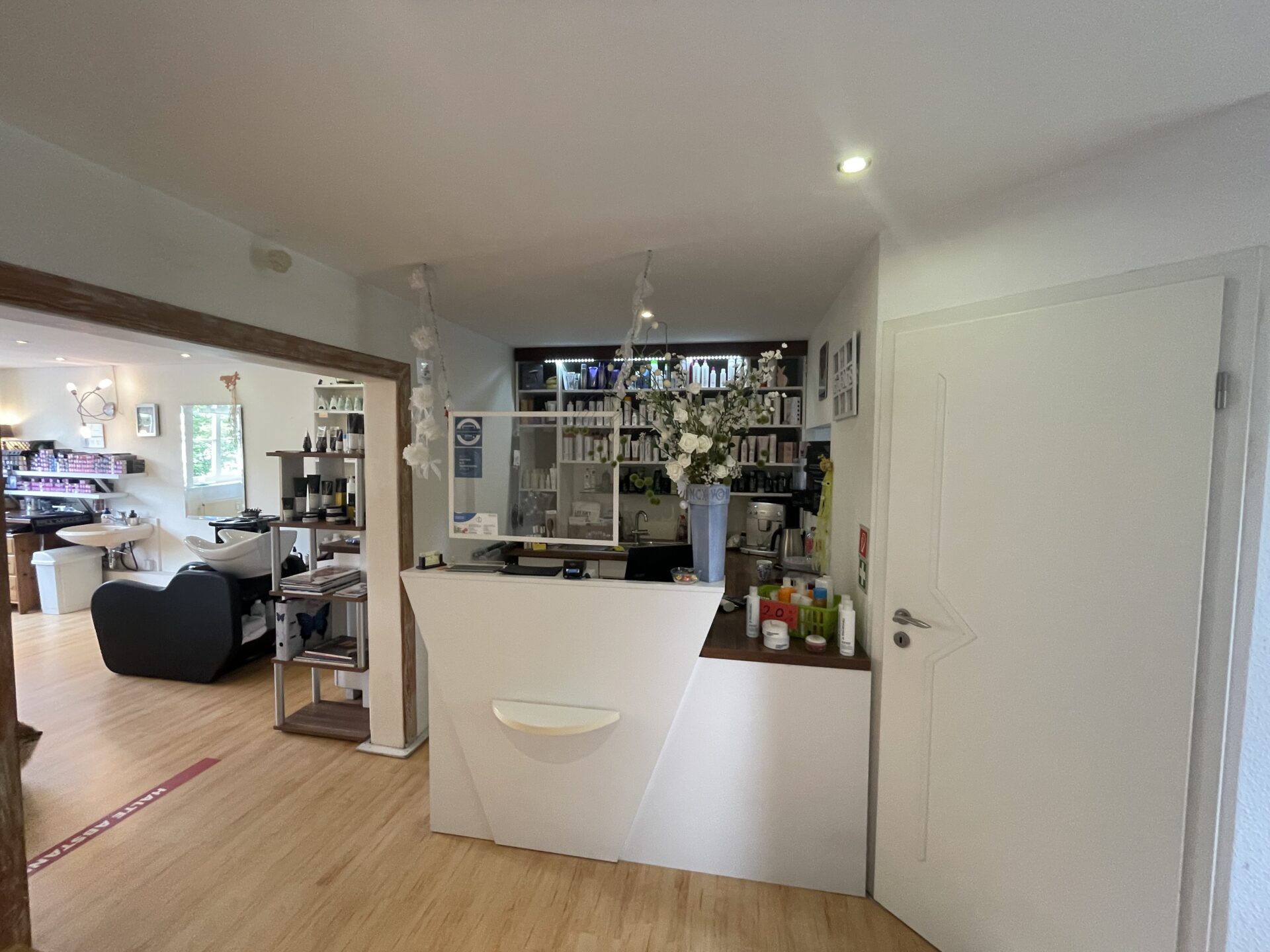 Empfangsbereich des Friseursalons mit Theke, Produkten und Dekoration im Hintergrund.