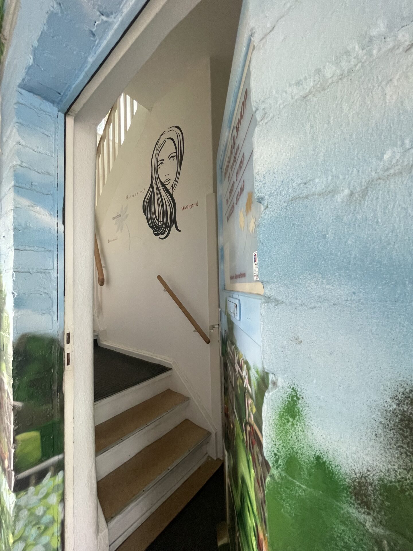 Blick durch die geöffnete Eingangstür auf Wandgestaltung mit Frauensilhouette und Begrüßung.