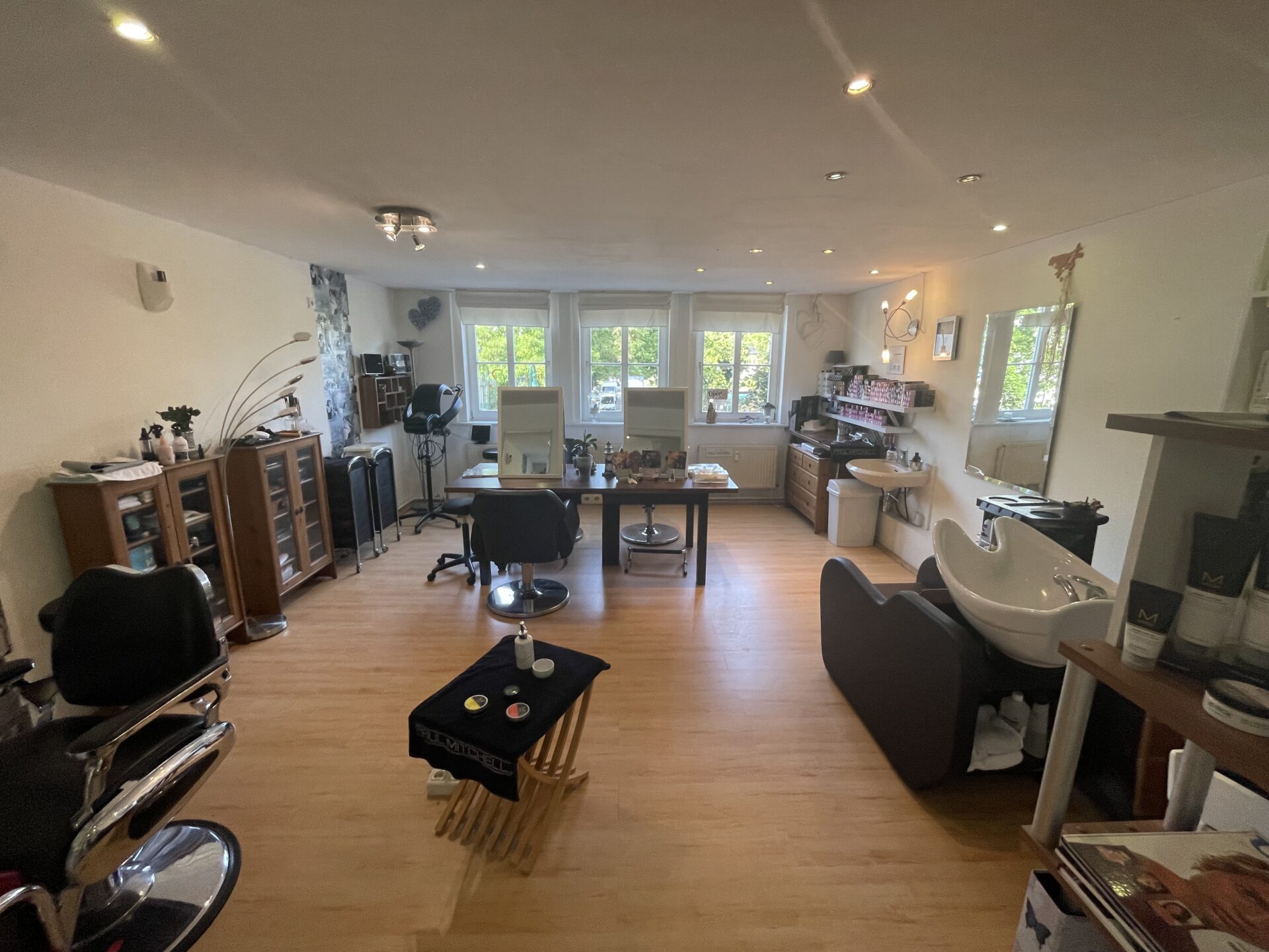 Blick in einen hellen Friseursalon mit mehreren Arbeitsplätzen, großen Fenstern und moderner Ausstattung.