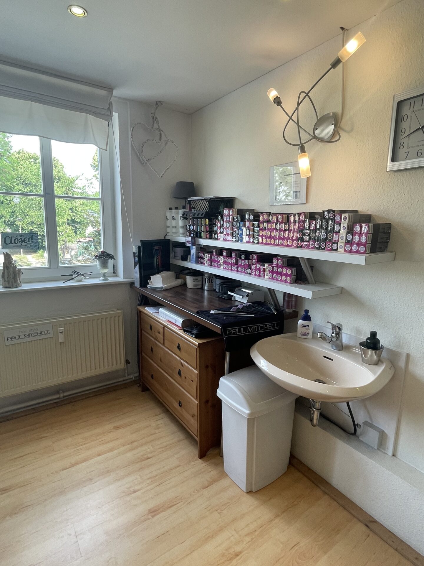 Detailaufnahme einer Farbmischstation im Friseursalon mit Wandregalen voller Haarfarben und Waschbecken.